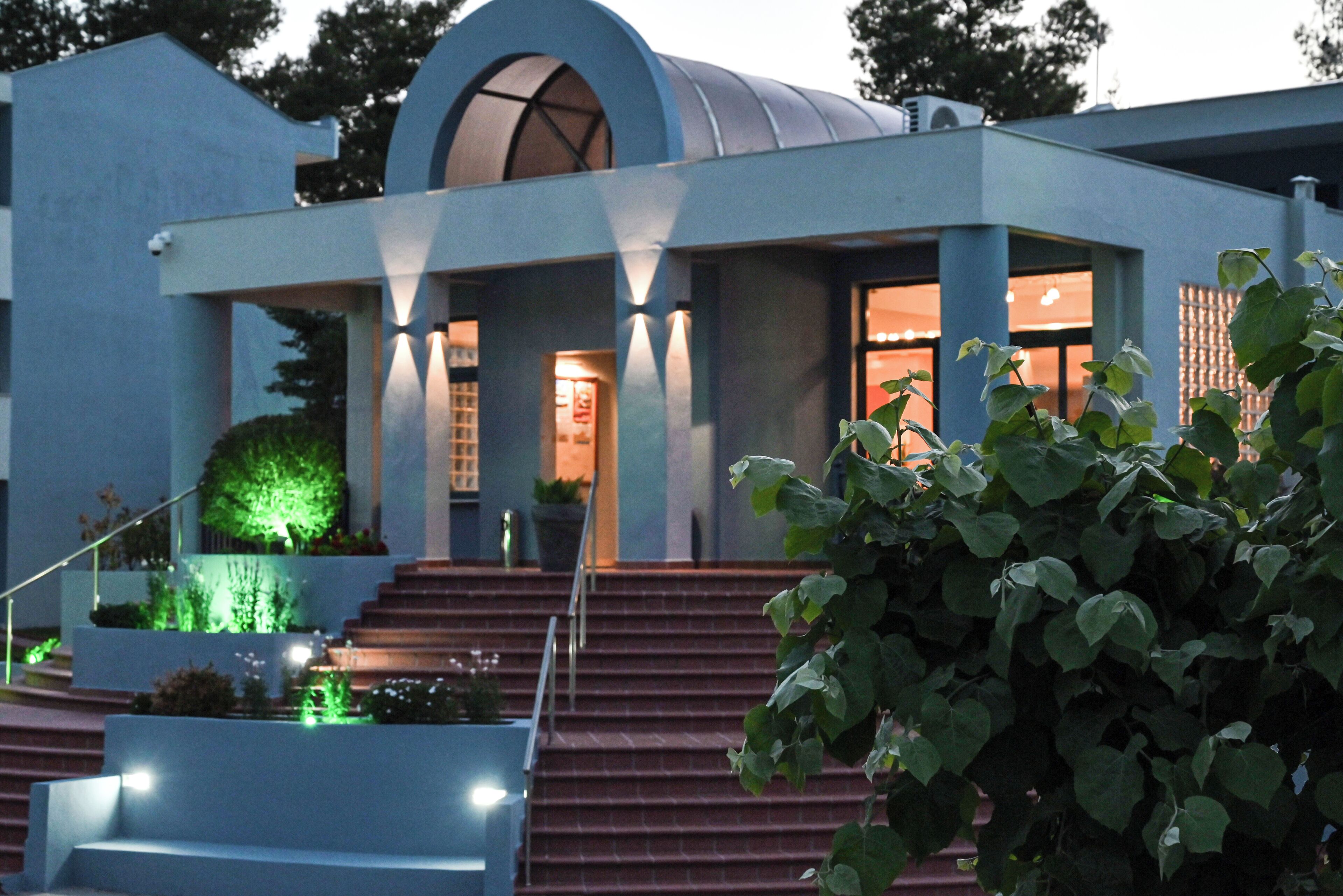 A modern building with a dome structure, steps leading to the entrance, and a well-lit facade.