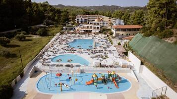 A large outdoor swimming pool with multiple lanes, surrounded by lounge chairs and umbrellas, and a playground area with slides and water features.