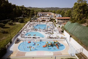 A large outdoor swimming pool with multiple lanes, surrounded by lounge chairs and umbrellas, and a playground area with slides and water features.