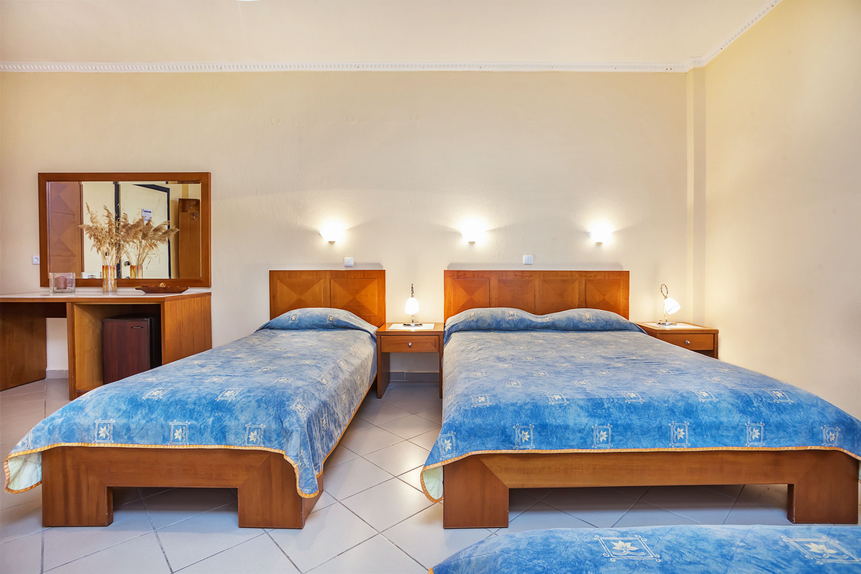 A hotel room with two wooden beds, a desk, and a mirror.