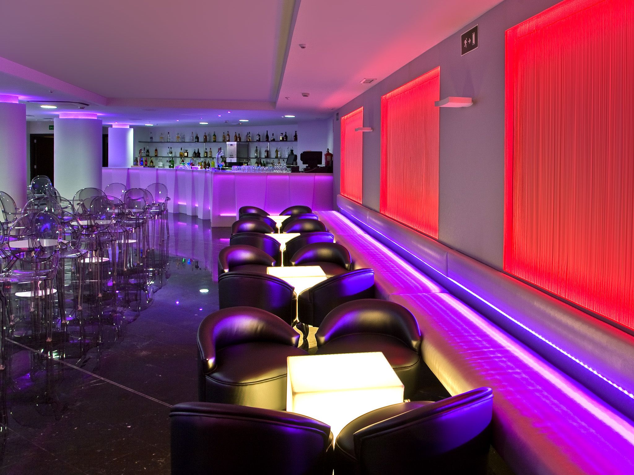 A modern bar area with a row of black leather chairs and a bar counter.