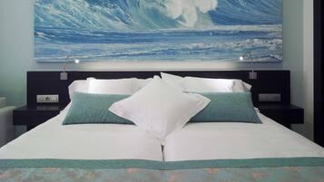 Une chambre avec un grand lit, deux tables de chevet et un tableau représentant une vague, accroché au mur.