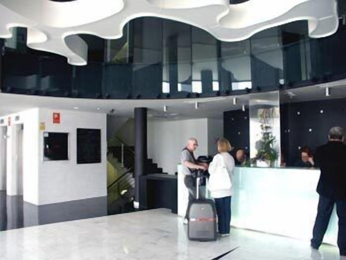 Un lobby moderno con un mostrador de recepción, una escalera y una barandilla de vidrio.