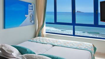 Une chambre à coucher avec un lit, une fenêtre donnant sur la mer et un tableau accroché au mur.
