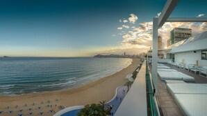 A beachfront hotel with a pool, sun loungers, and a view of the ocean and city skyline. - Villa del Mar Hotel (Benidorm)