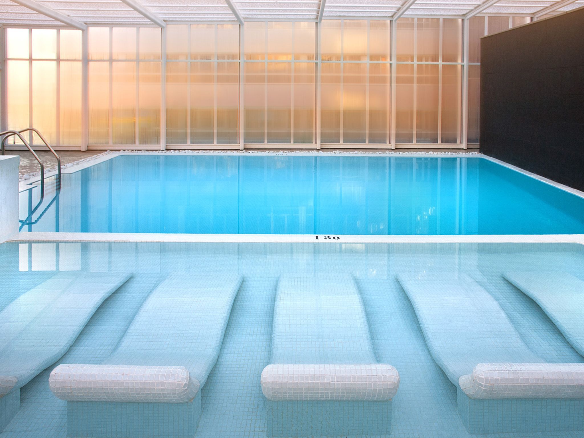 An indoor swimming pool with clear water, a tiled floor, and a glass ceiling.