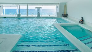 A large indoor swimming pool with clear blue water, a separate hot tub area, and a view of the sea through large windows. - Villa del Mar Hotel (Benidorm)