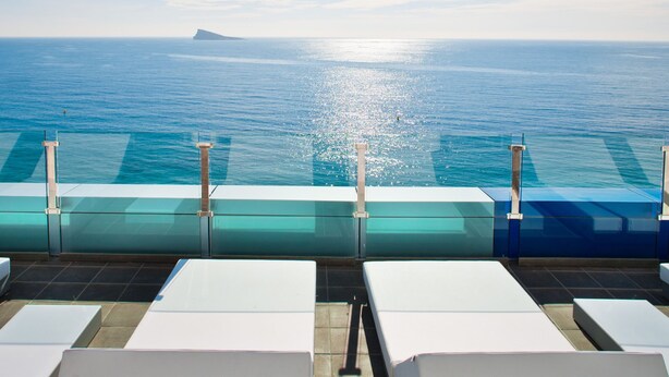 A poolside area with lounge chairs and a view of the ocean. - Villa del Mar Hotel (Benidorm)