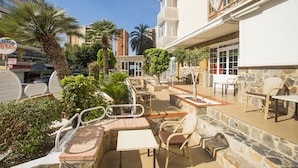 An outdoor patio area with stone seating, palm trees, and a view of the cityscape.