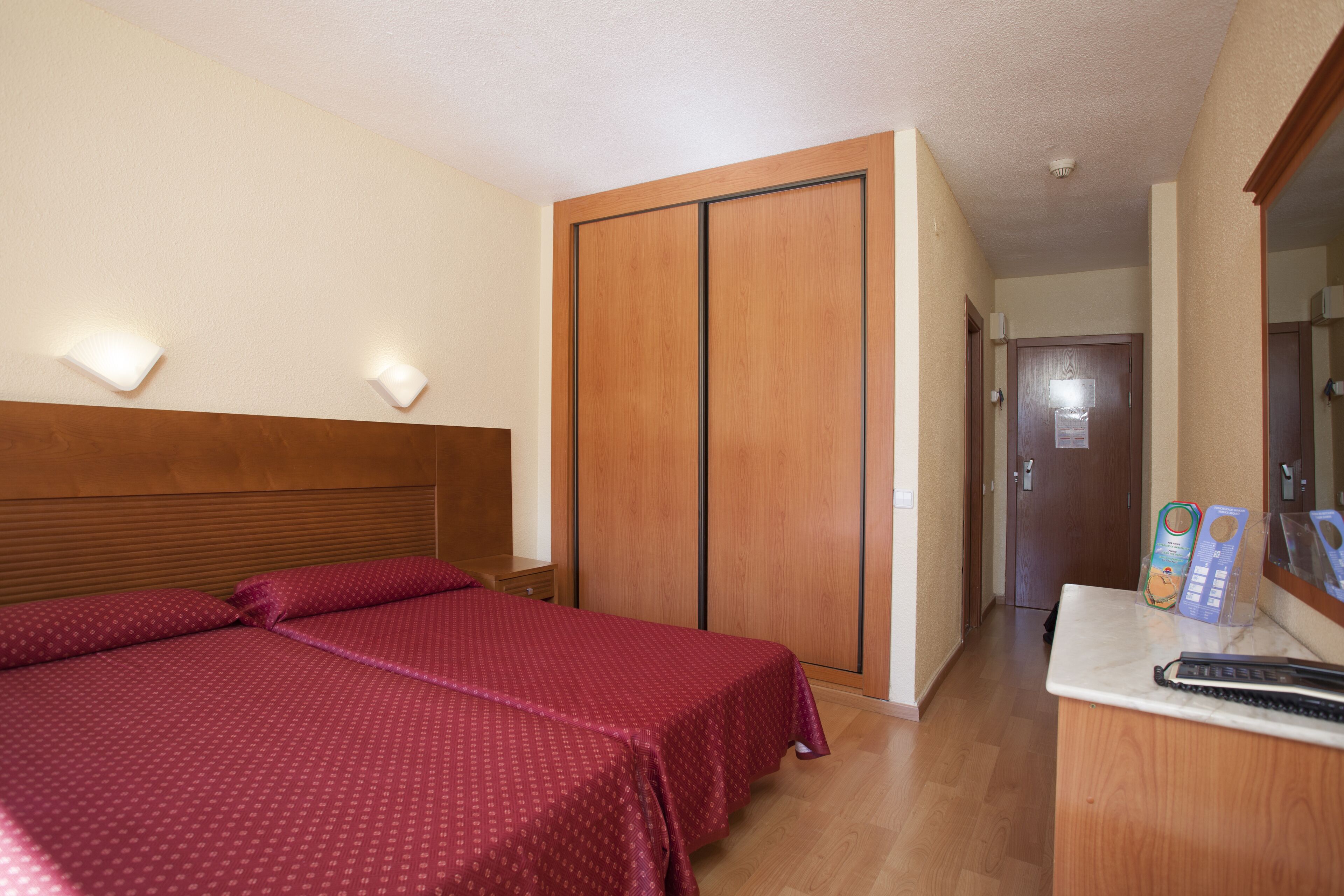 A hotel room with a bed, a wooden wardrobe, a desk with a keyboard, and a mirror.