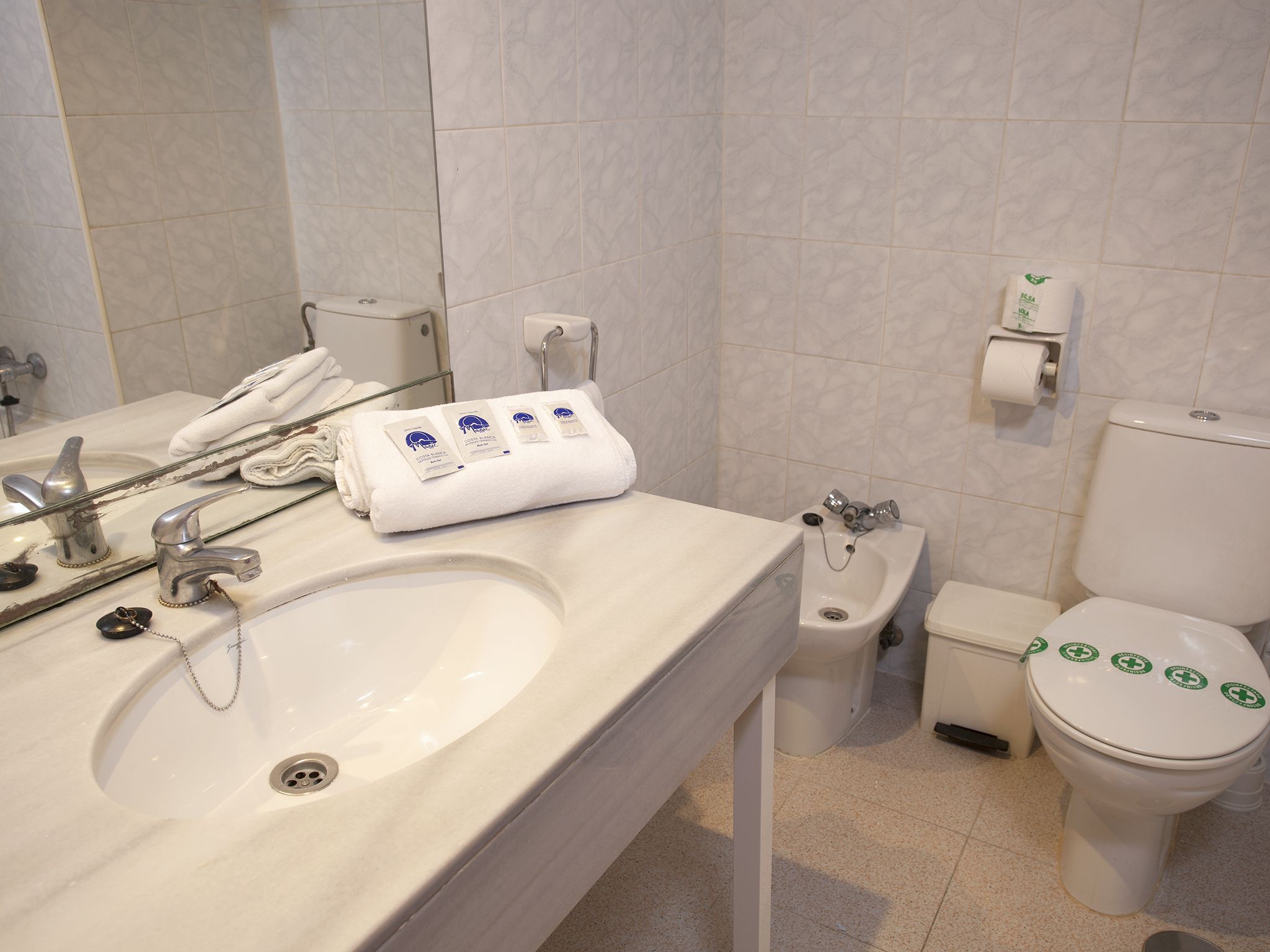 Un baño con lavamanos, espejo, toallero, inodoro y bidé.