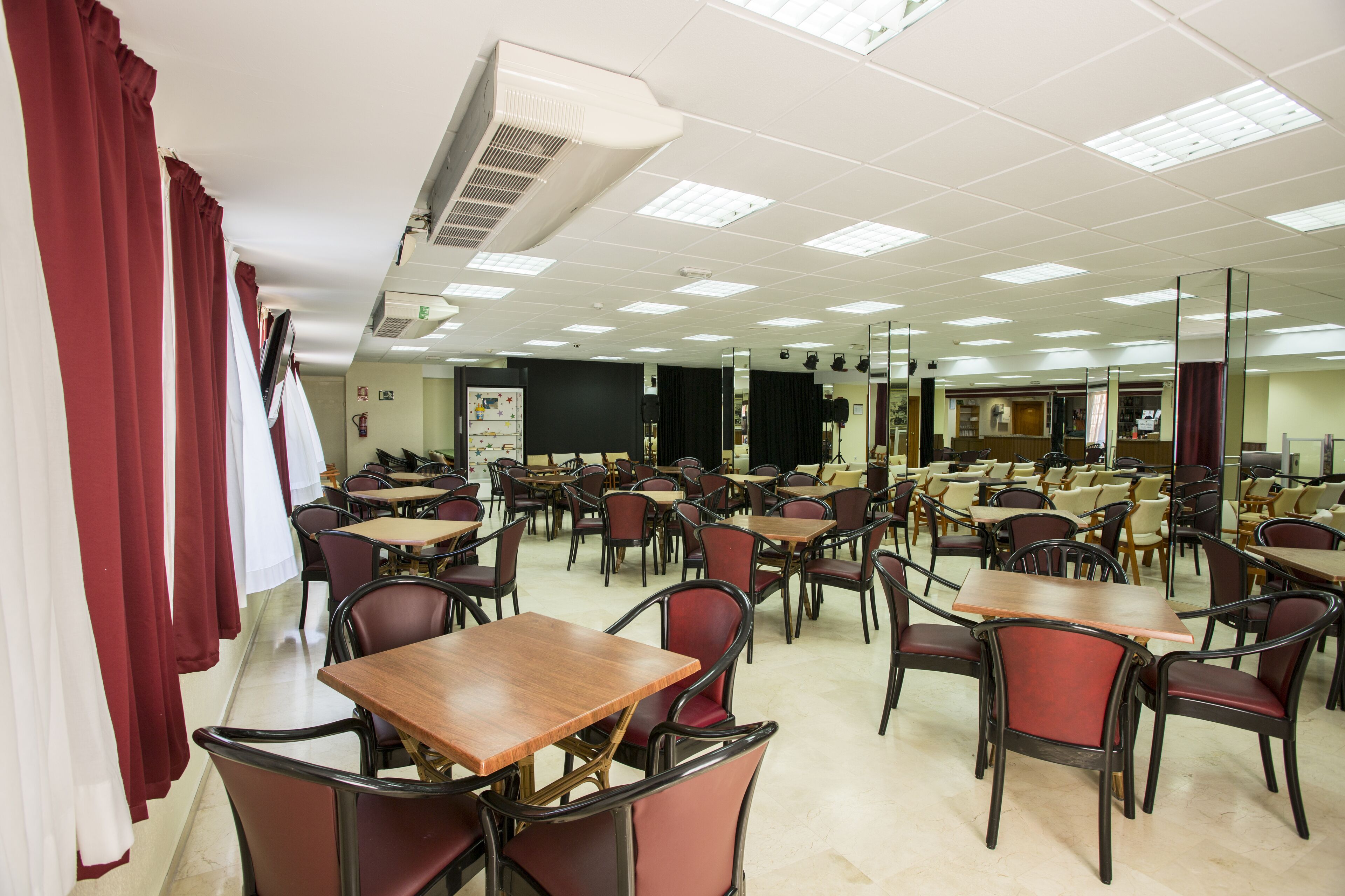 A spacious dining area with multiple tables and chairs, a ceiling air conditioning unit, and a blackboard in the background.