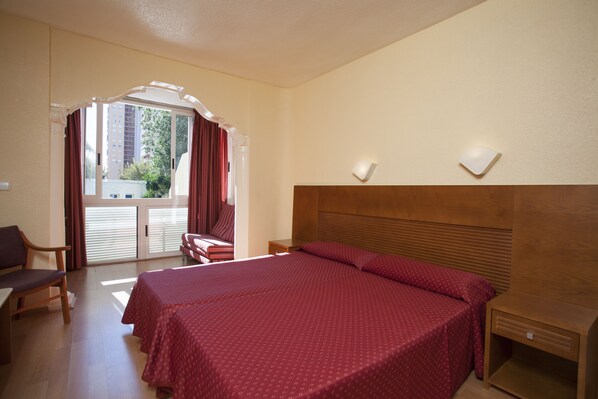 A hotel room with a large bed, a desk, a chair, and a view of the outside.