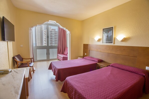 A hotel room with two beds, a desk, a chair, a TV, and a window with curtains.