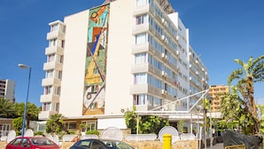 A multi-story hotel with a distinctive mural on one side, balconies, and a covered outdoor seating area.