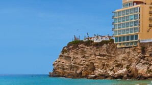 Un hôtel perché sur une falaise, surplombant la mer, avec de nombreux étages et des balcons offrant une vue sur la côte.