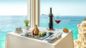 Une table dressée avec une bouteille de vin, un verre de vin rouge, une assiette de nourriture, une serviette et une petite plante.