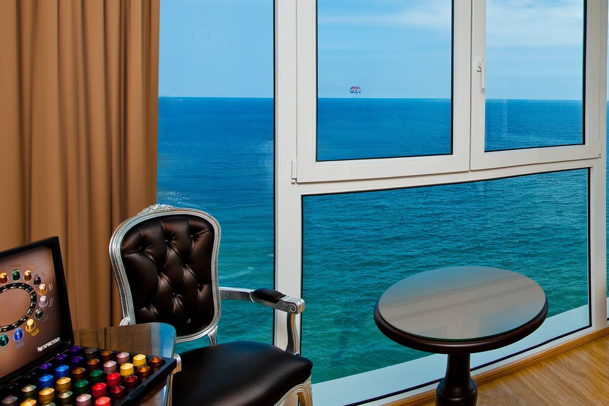 Ein Zimmer mit großem Fenster mit Meerblick, ein Ledersessel, ein kleiner runder Tisch und eine Nespresso-Kaffeemaschine.