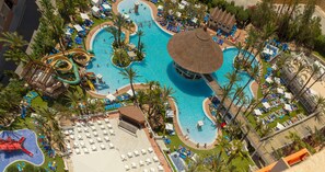 An aerial view of a resort with a large central pool, multiple water slides, and numerous sun loungers and umbrellas.