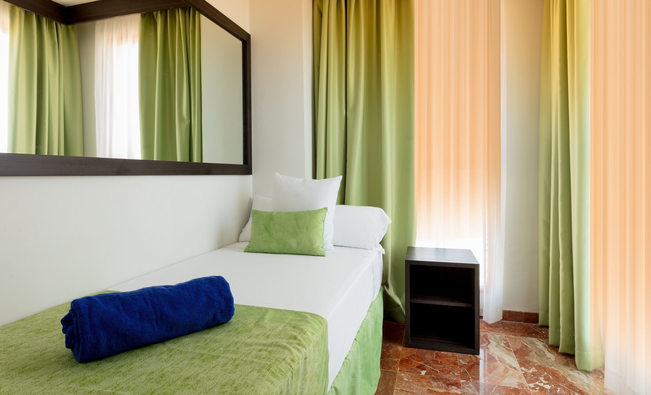 A hotel room with a bed, a small bedside table, and green curtains.