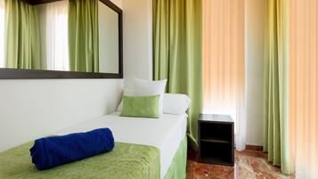A hotel room with a bed, a small bedside table, and green curtains.