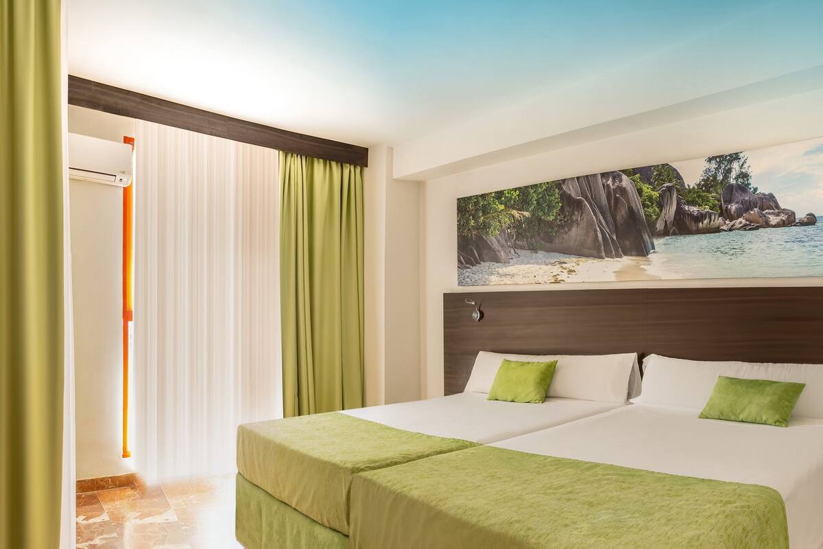 Habitación de hotel con cama, televisión, teléfono y un cuadro de una playa.