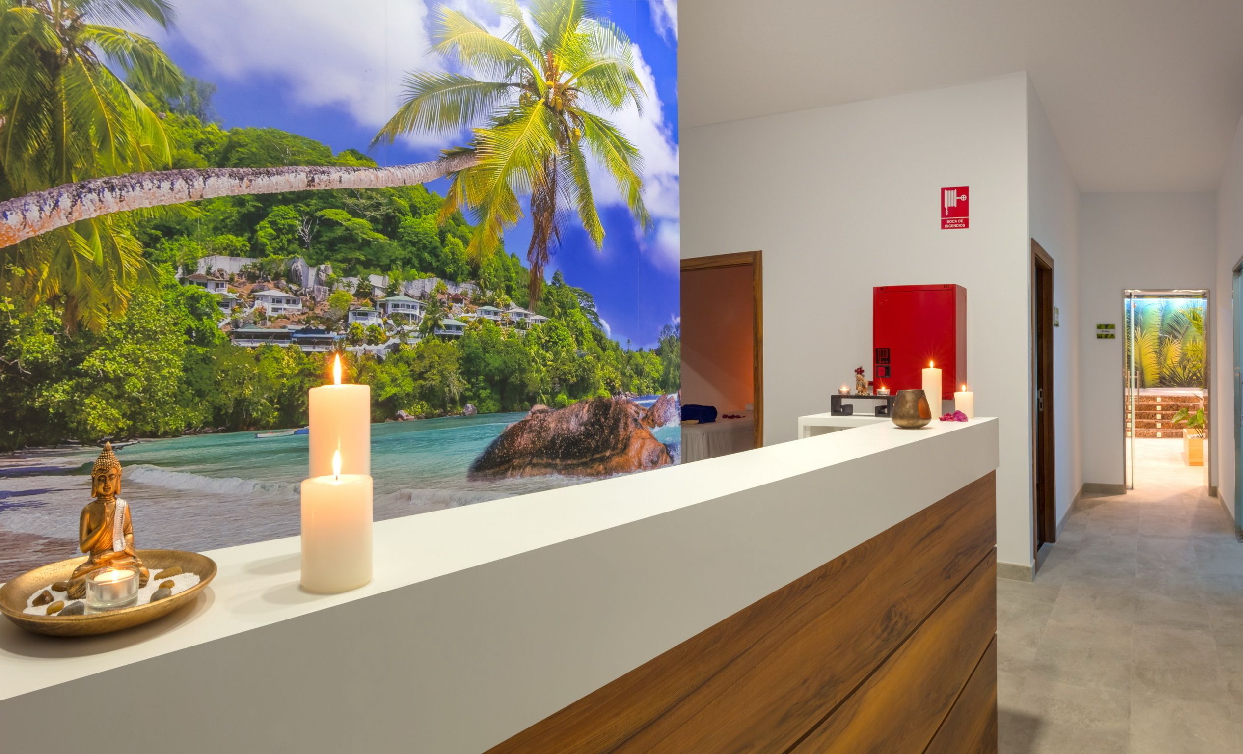 A reception desk with a mural of a tropical beach, a Buddha statue, and candles.