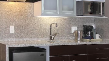 Una cocina con encimeras de granito, un lavamanos de acero inoxidable, una cafetera y un microondas.