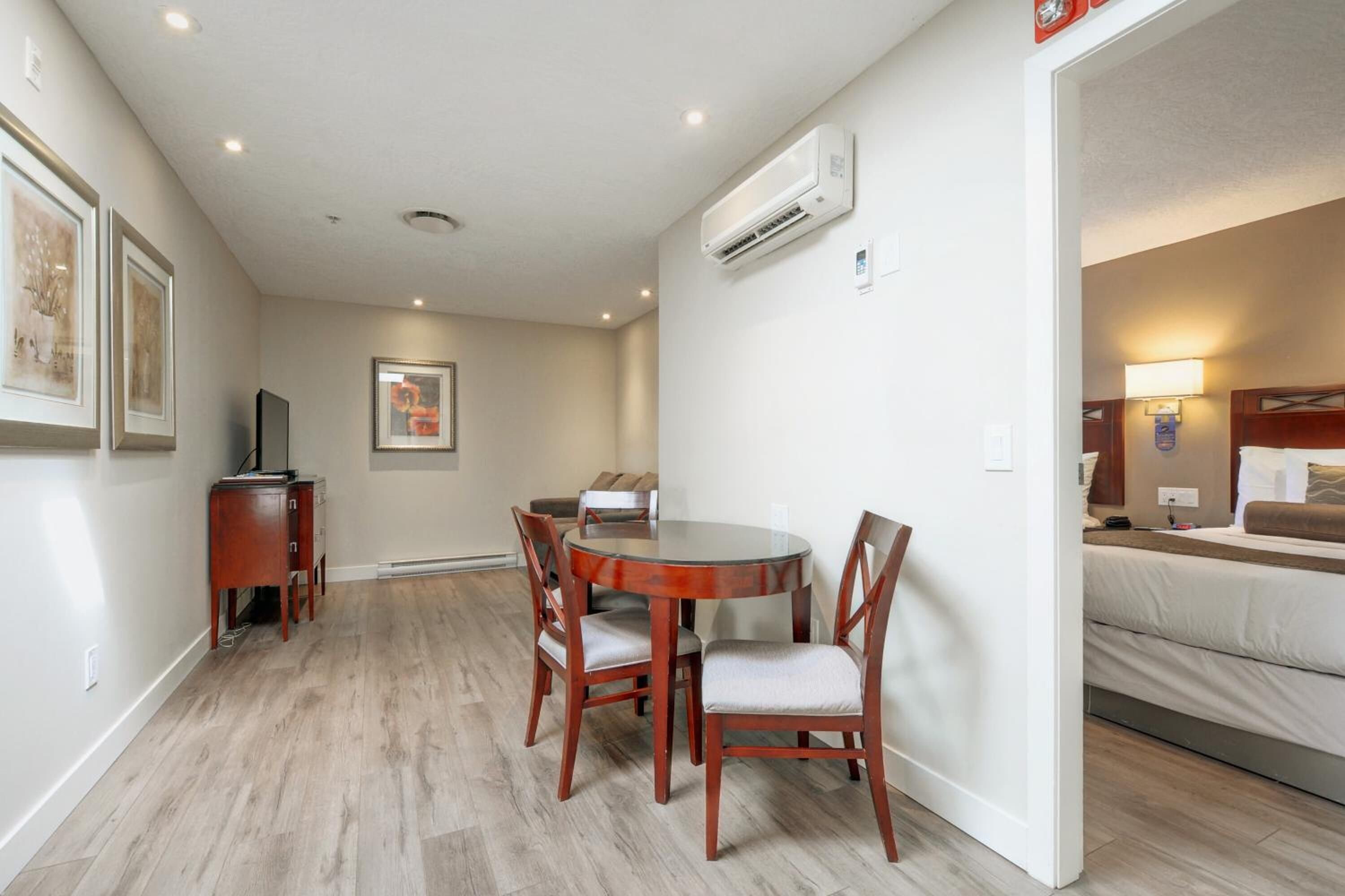 A hotel room with a bed, a desk with a chair, a dining table with chairs, and a TV.