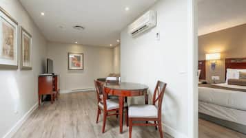 A hotel room with a bed, a desk with a chair, a dining table with chairs, and a TV.