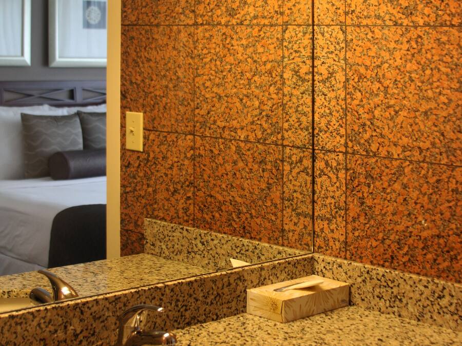 Un baño con encimera de granito, lavamanos y espejo.