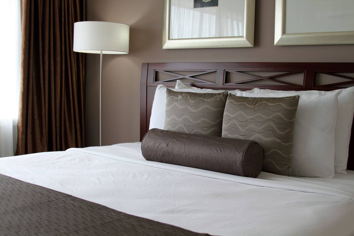 A neatly made bed with a headboard, a lamp, and framed pictures on the wall.