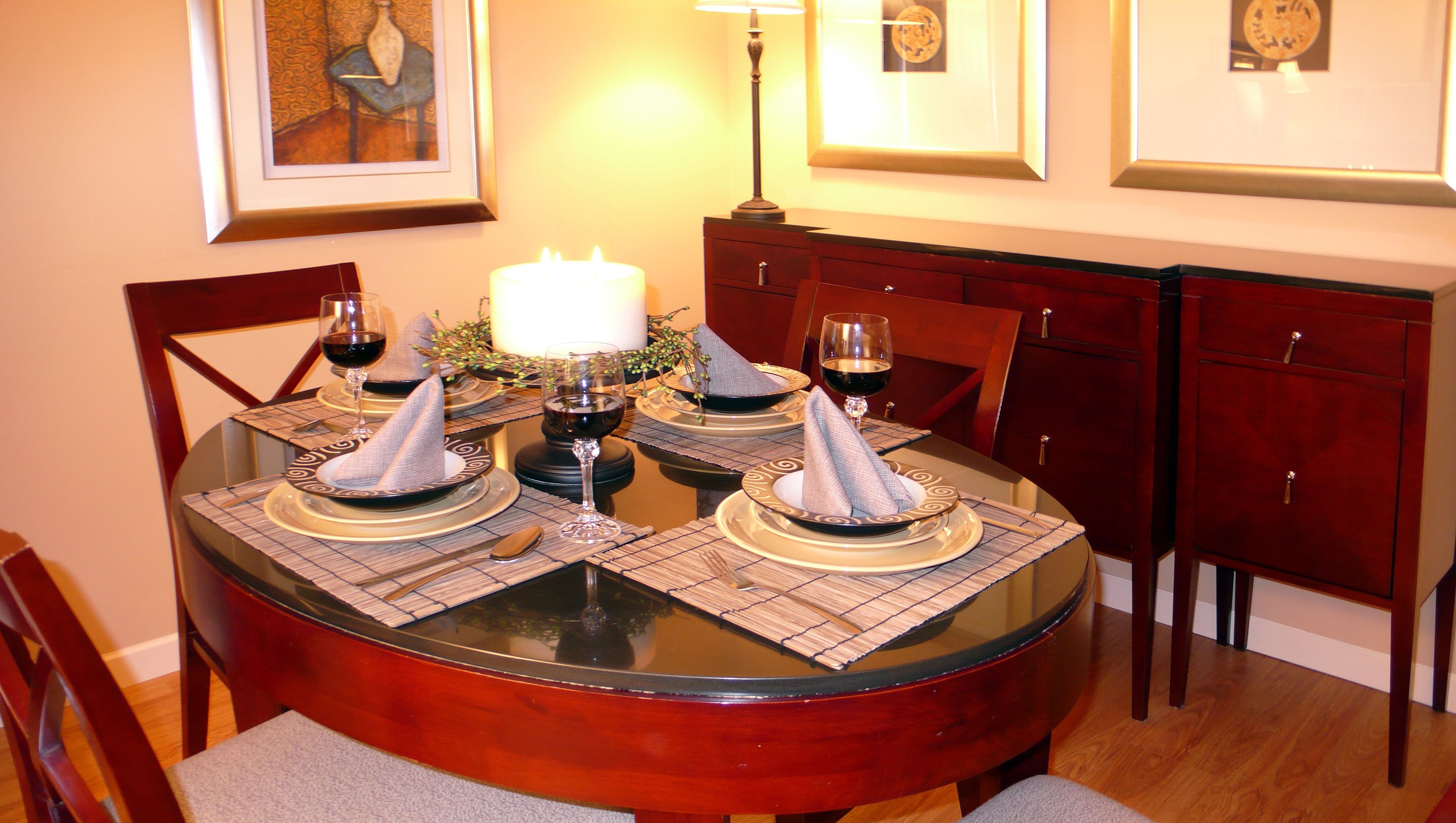 Una mesa de comedor lista para cuatro, con individuales, copas de vino y una vela.