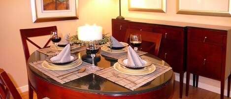 Una mesa de comedor lista para cuatro, con individuales, copas de vino y una vela.