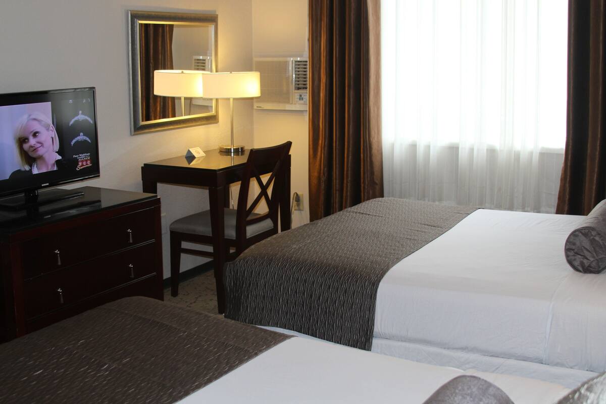 A hotel room with a bed, a desk with a chair, a television, a lamp, and a window with curtains.