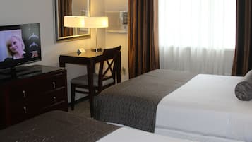 Une chambre d’hôtel comprenant un lit, un bureau avec une chaise, une télévision, une lampe et une fenêtre avec des rideaux.