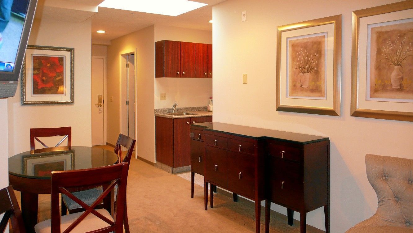 A dining area with a glass table and chairs, wooden cabinets, and two framed artworks on the wall.