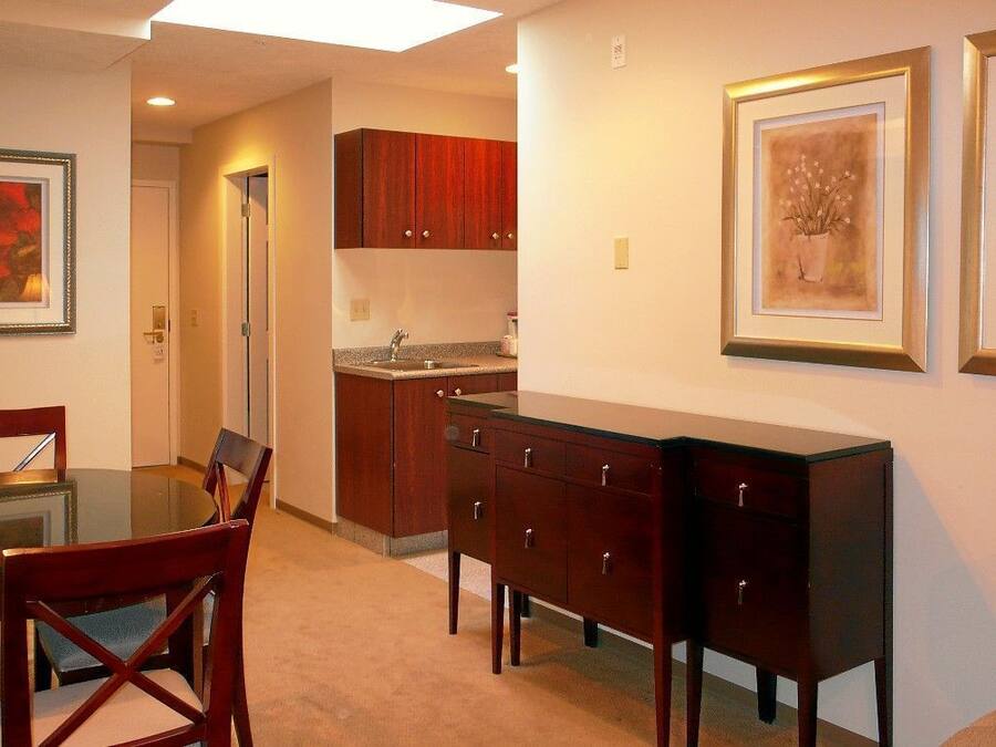 A dining area with a glass table and chairs, wooden cabinets, and two framed artworks on the wall.