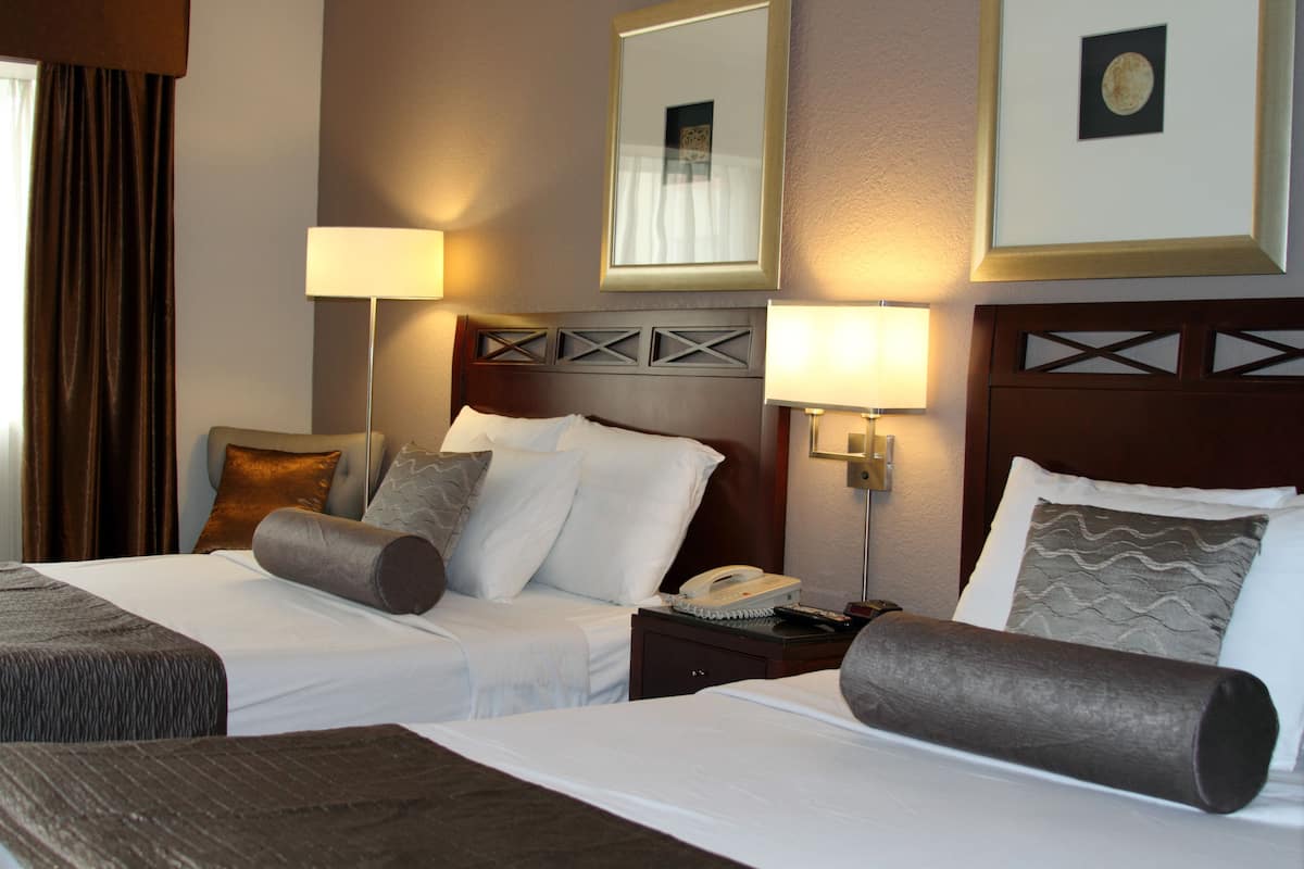 A hotel room with two beds, a nightstand, a lamp, and a framed picture on the wall.