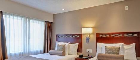 Une chambre d’hôtel avec deux lits, une table de chevet, une lampe et une fenêtre avec des rideaux.