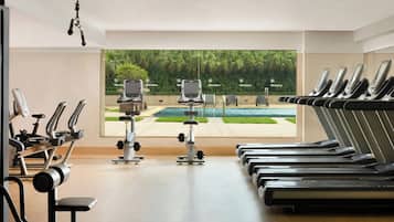 Ein Fitnessstudio mit Laufbändern, Ergometer und Krafttrainingsgeräten, mit Blick auf einen Pool und Grünflächen.