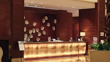 Zona de recepción con un mostrador de madera, un panel decorativo en la pared y una planta en maceta.