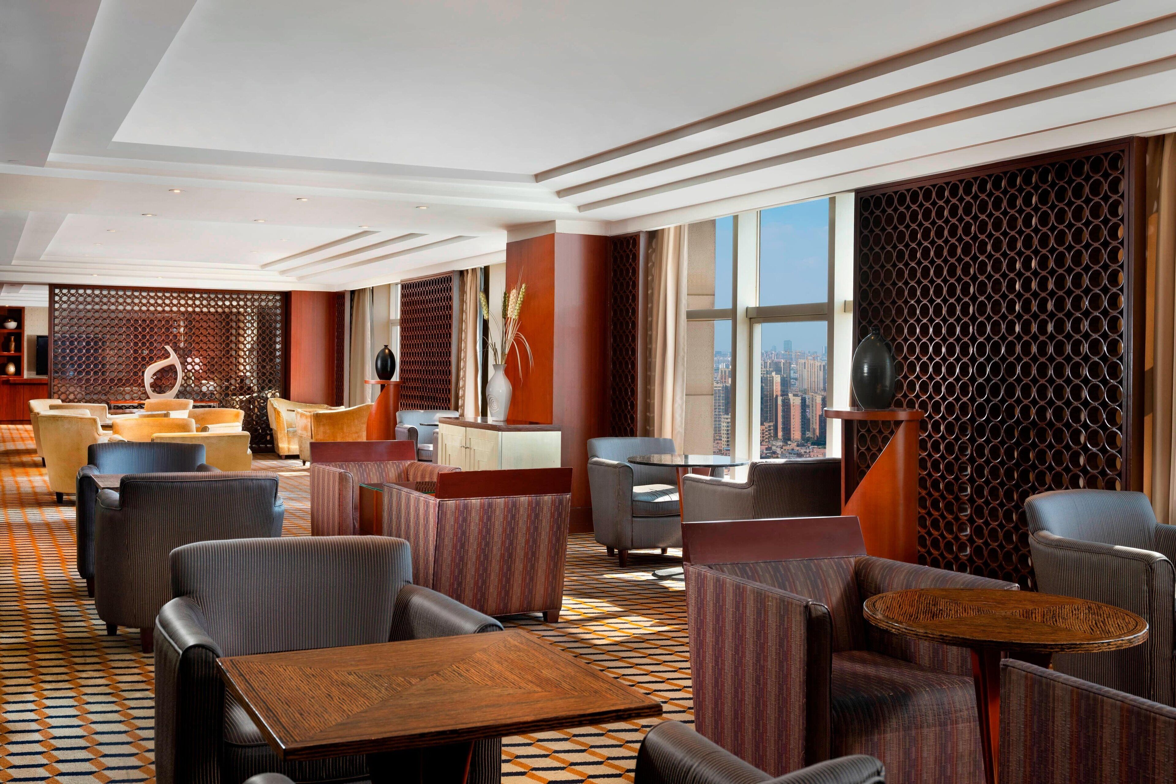 A modern hotel lobby with a patterned floor, seating areas, and large windows offering a city view.
