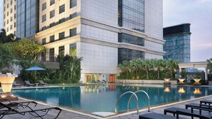 A hotel pool area with lounge chairs, a swimming pool, and a building with a modern design.