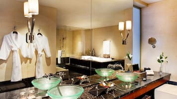 A modern bathroom with a large mirror, two glass bowls on the vanity, and a robe rack with two white robes.