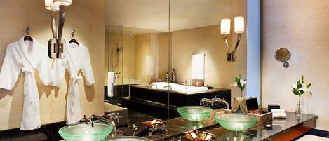 A modern bathroom with a large mirror, two glass bowls on the vanity, and a robe rack with two white robes.