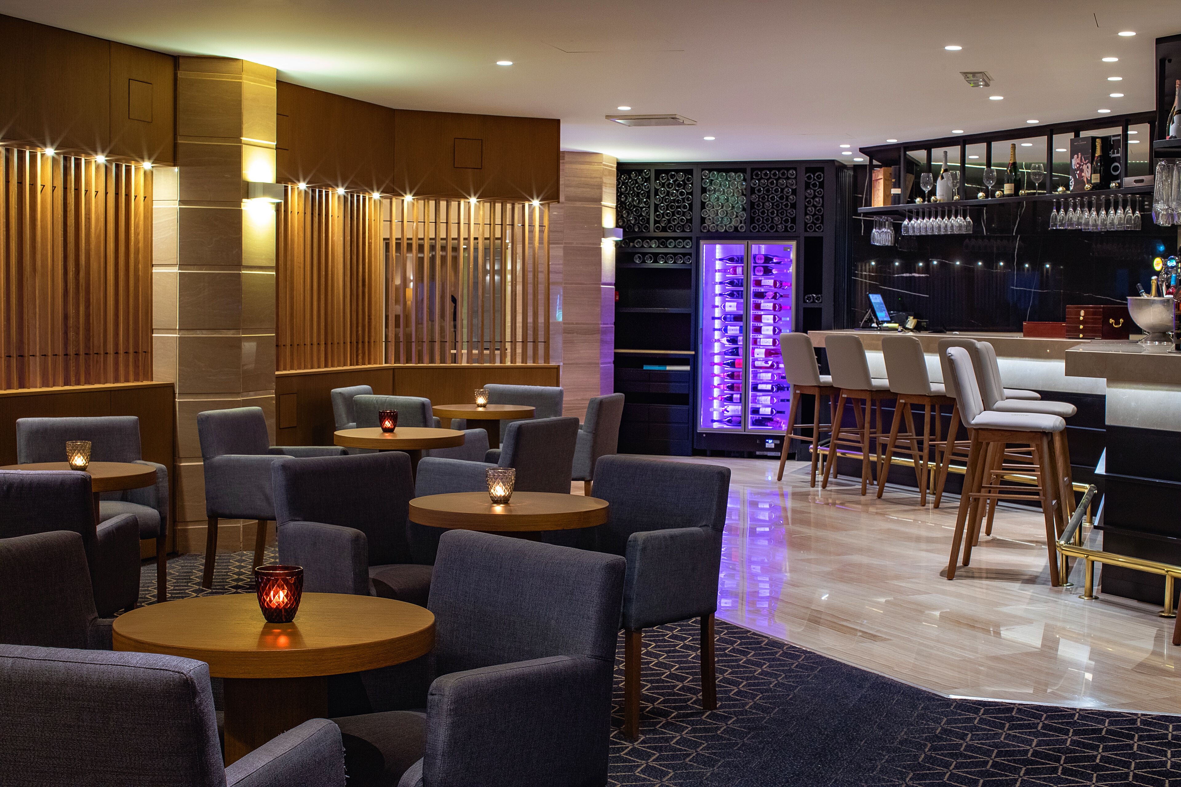 Uma área de bar moderna com mesas redondas, banquetas e um display de vinhos.