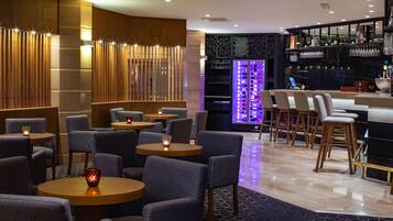 Uma área de bar moderna com mesas redondas, banquetas e um display de vinhos.