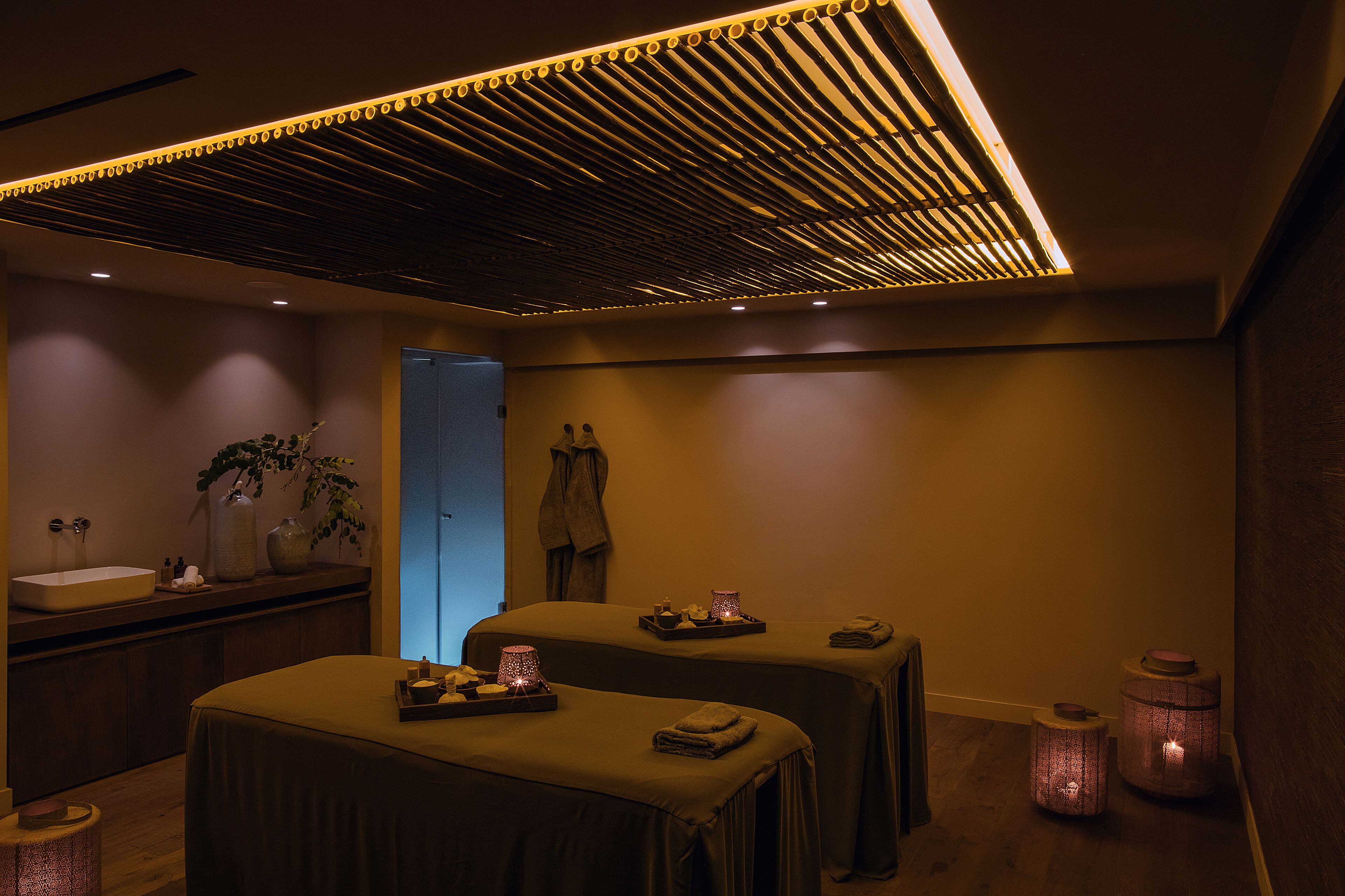 Un cuarto de spa con dos camillas de masaje, un lavamanos y velas decorativas.