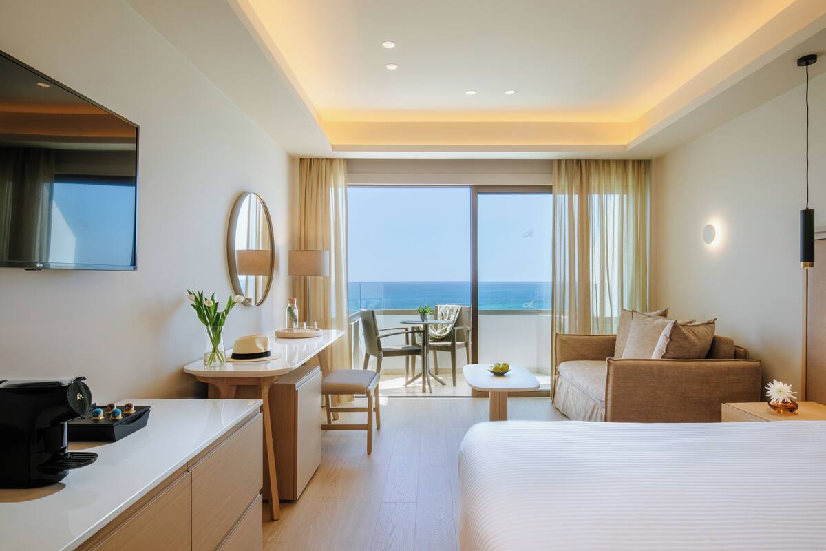 Une chambre d’hôtel comprenant un lit, un bureau, une chaise, une petite table et un balcon avec vue sur l’océan.
